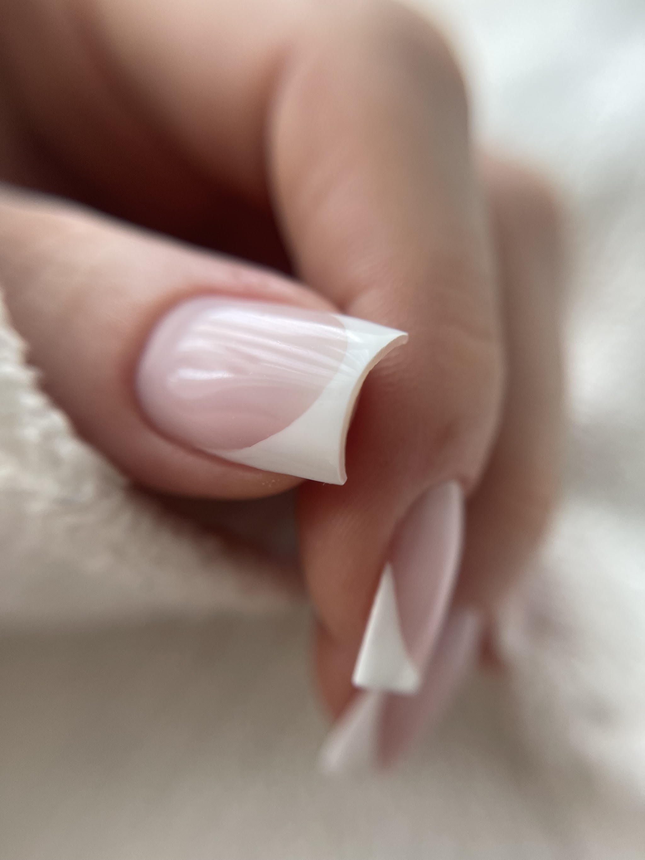 Nagels met een witte French tip, op een crèmekleurige gebreide trui