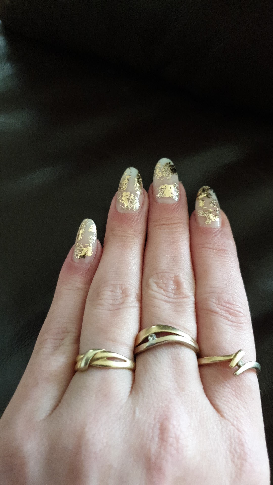 Nagels met goudfolie op een hand met gouden ringen